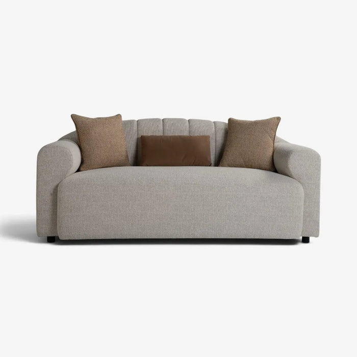 A modern low-profile loveseat sofa upholstered in light gray textured fabric, styled with three throw pillows in brown and taupe, set against a plain white background.