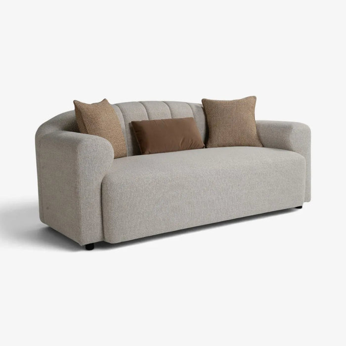 A modern curved two-seater sofa upholstered in light beige textured fabric, styled with three throw pillows in beige and brown, set against a plain white background.