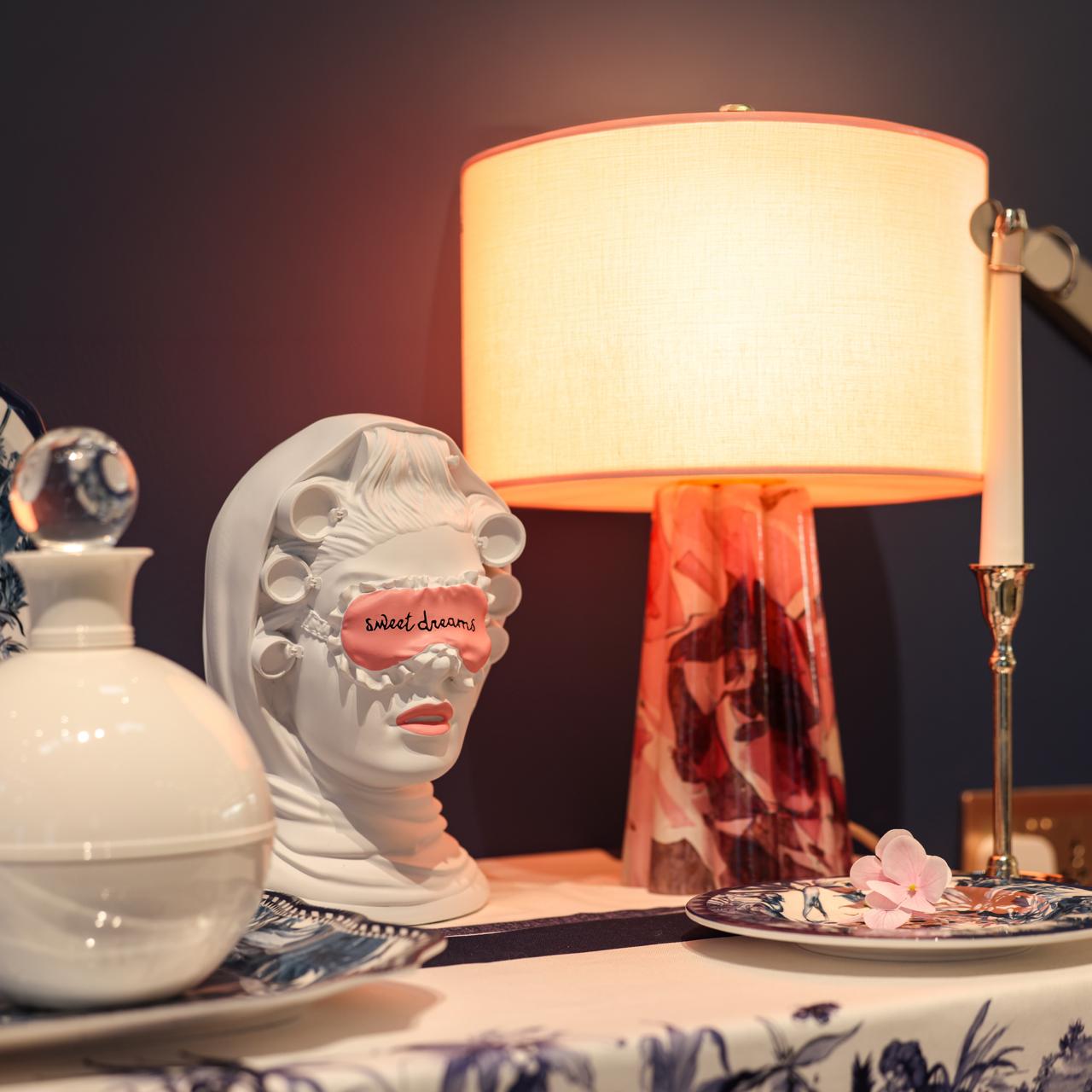 Decorative head with pink bow, lamp, and candle on a table with a dark background