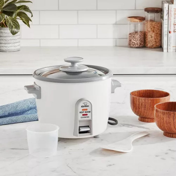 White rice cooker on a kitchen counter with wooden bowls and a plant in the background.