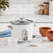 White rice cooker on a kitchen counter with wooden bowls and a plant in the background.