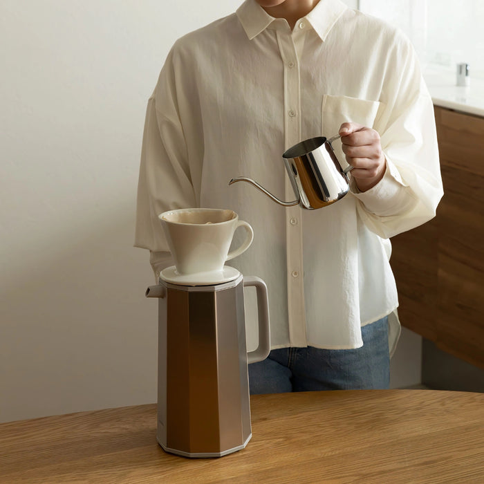 Person making coffee using a pour-over setup on a wooden table.
