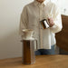 Person making coffee using a pour-over setup on a wooden table.
