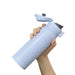 Hand holding a light blue water bottle with a black cap on a white background
