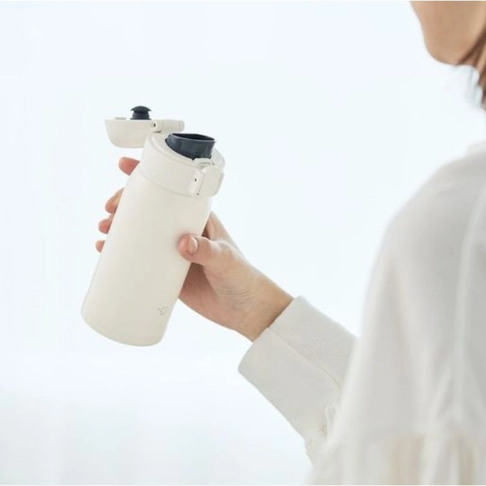 Person holding a white water bottle with a black cap on a light gray background
