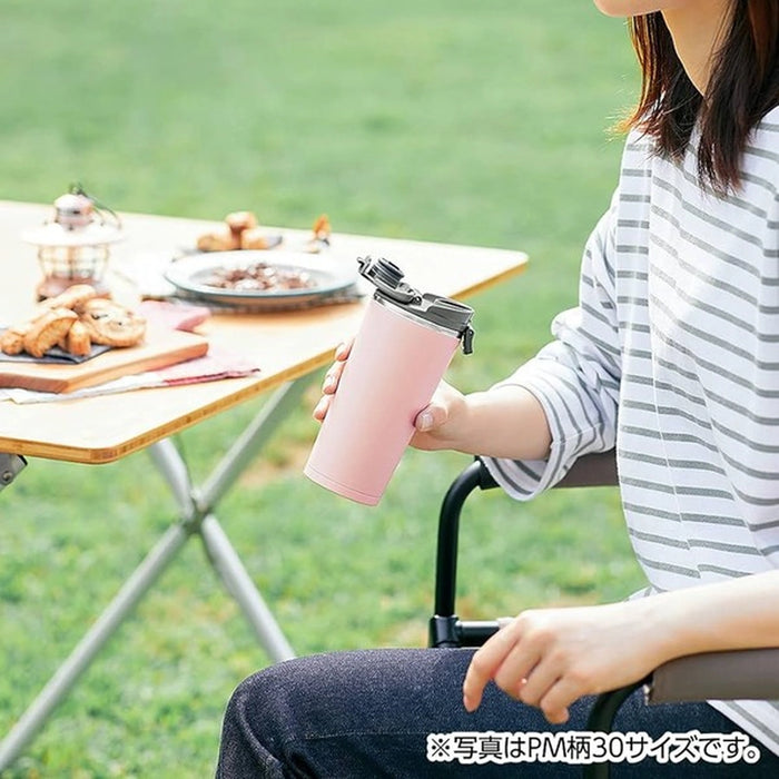 Person holding a pink insulated mug outdoors at a picnic table.