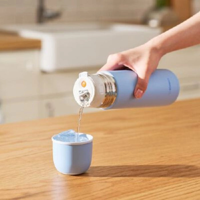 Person pouring water from a blue thermos into a matching cup on a wooden surface.