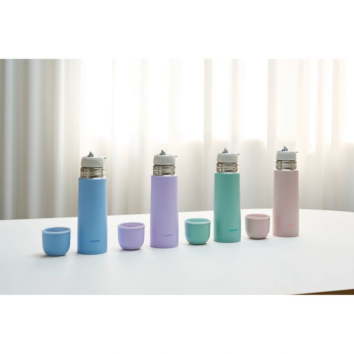 Set of colorful water bottles and cups on a white surface with a light curtain background