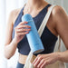 Person holding a blue cylindrical product with a strap over shoulder