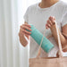 Person holding a turquoise water bottle and beige tote bag against a light background