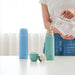 Person pouring water from a glass into a teal thermos with a white background