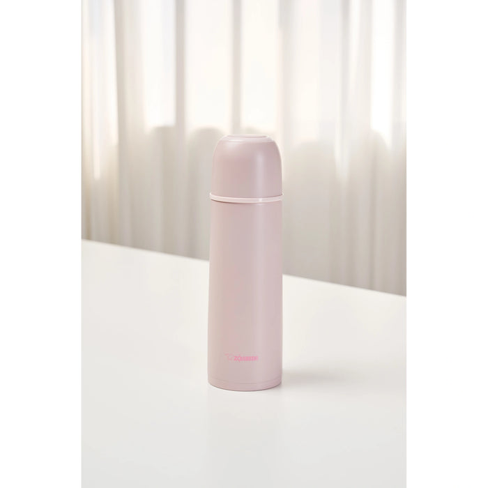 Pink thermos bottle on a white surface with a light curtain background
