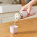Person pouring water from a pink thermos into a small white cup on a wooden surface.