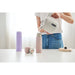 Person pouring water from a white electric kettle into a pink thermos on a white surface.