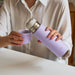 Person holding a purple water bottle and small container, wearing a white shirt.