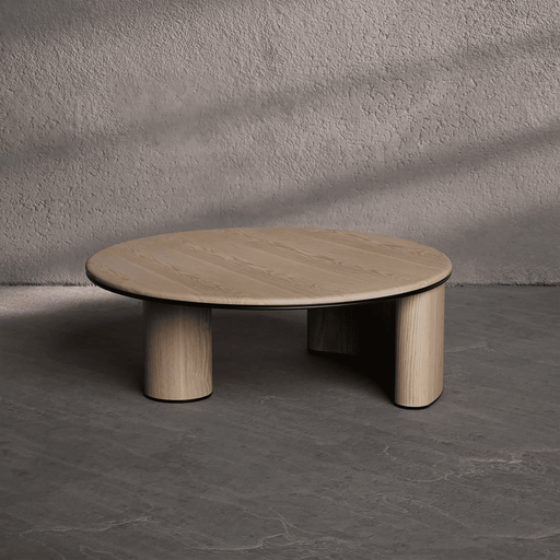 Wooden coffee table with three cylindrical legs on a gray floor against a gray wall