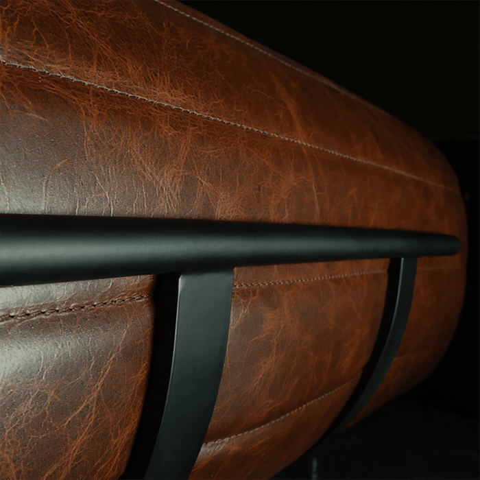 Close-up of a brown leather chair with a black metal armrest on a dark background