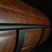 Close-up of a brown leather chair with a black metal armrest on a dark background
