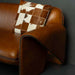 Brown leather sofa with a checkered pillow against a gray wall
