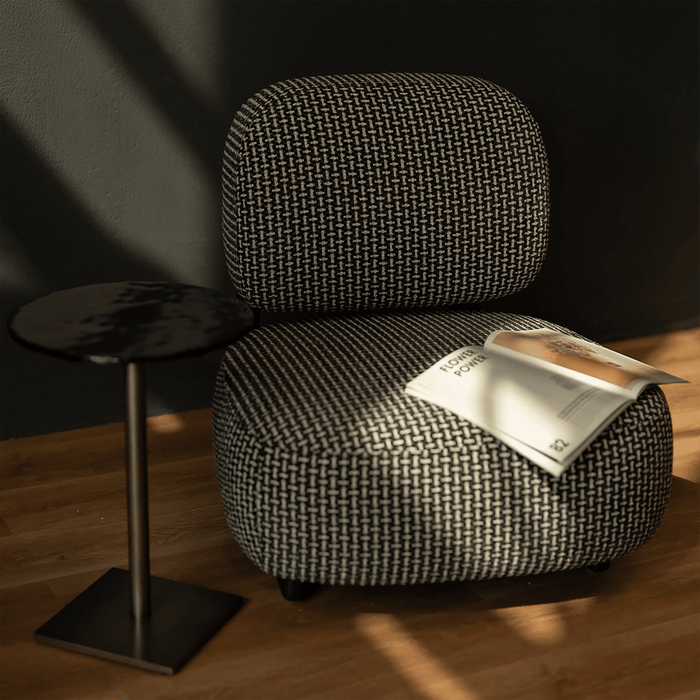 Textured armchair with a magazine on a wooden floor next to a small table.