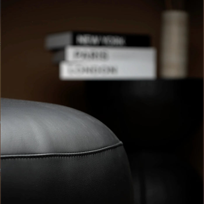 Close-up of a gray leather armchair with a blurred background featuring books.