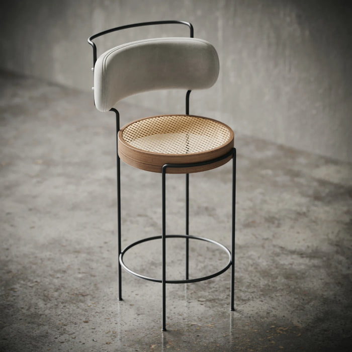 Modern bar stool with woven seat and upholstered backrest on a concrete floor.
