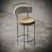 Modern bar stool with woven seat and upholstered backrest on a concrete floor.