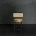 Bar stool with beige cushioned seat and backrest against a dark gray wall