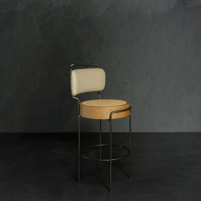 Bar stool with beige cushioned seat and backrest against a dark gray wall.