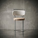 Modern bar stool with cushioned seat and backrest against a textured wall.