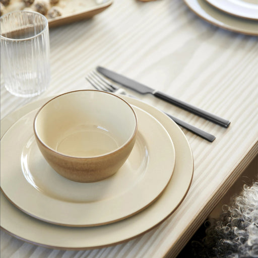 Dining table setting with beige ceramic bowls and plates on a textured tablecloth.
