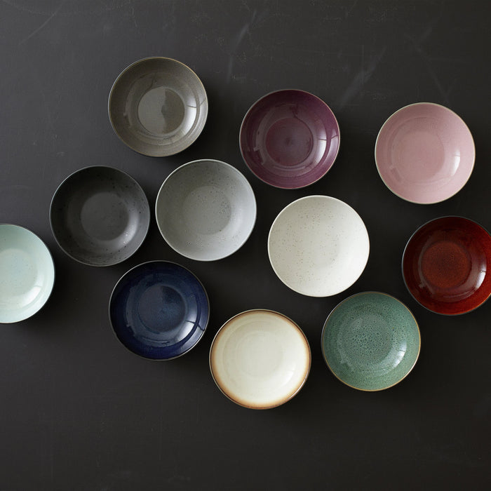 Collection of ceramic plates in various colors on a dark surface