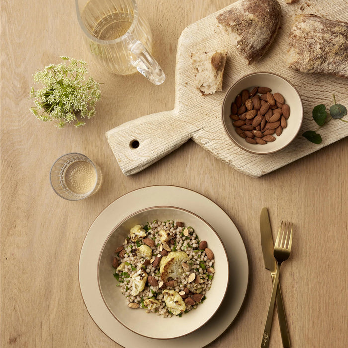 Table setting with a bowl of salad, bread, and almonds on a wooden table.