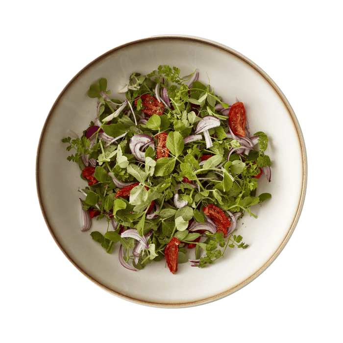 Green salad with red peppers and onions in a white bowl on a white background
