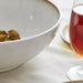Glass of red wine next to a white bowl on a light surface