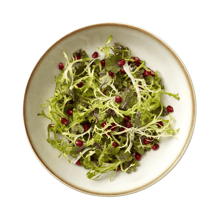 Green salad with pomegranate seeds on a white plate with a brown rim.