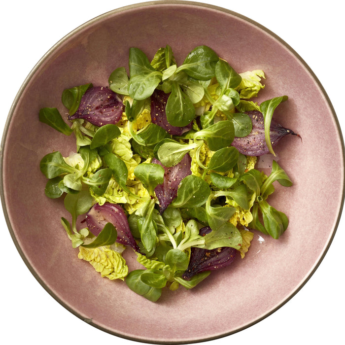 Salad with green leaves and purple onions on a pink plate