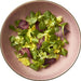 Salad with green leaves and purple onions on a pink plate