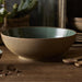 Brown ceramic bowl on a wooden surface with wooden spoons and small stones.