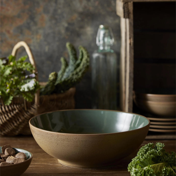Brown ceramic bowl on a wooden surface with greenery and a dark background