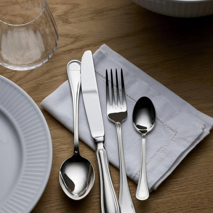 Silver cutlery set on a wooden table with a white plate and glass.