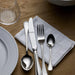 Silver cutlery set on a wooden table with a white plate and glass.