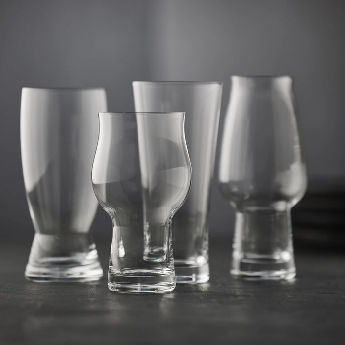 Four clear glass drinking glasses of different shapes on a dark surface with a dark background