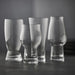 Four clear glass drinking glasses of different shapes on a dark surface with a dark background
