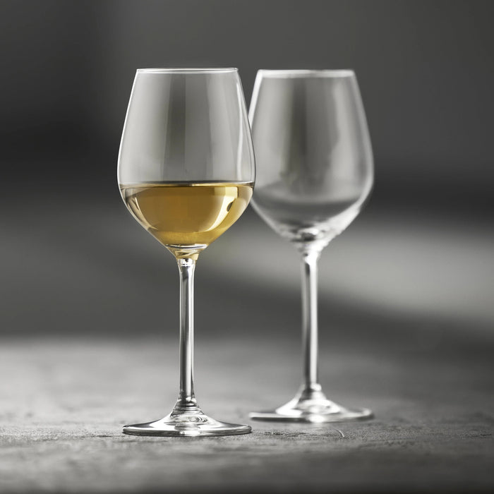 Two wine glasses, one filled with white wine, on a dark surface.