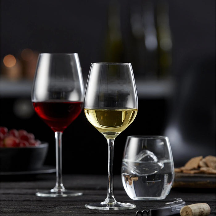 Two wine glasses with red and white wine, a small glass with a design, and a bottle in the background.