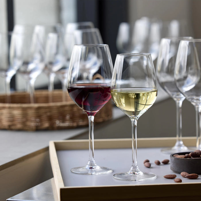 Two wine glasses, one with red wine and one with white wine, on a tray with more wine glasses in the background.