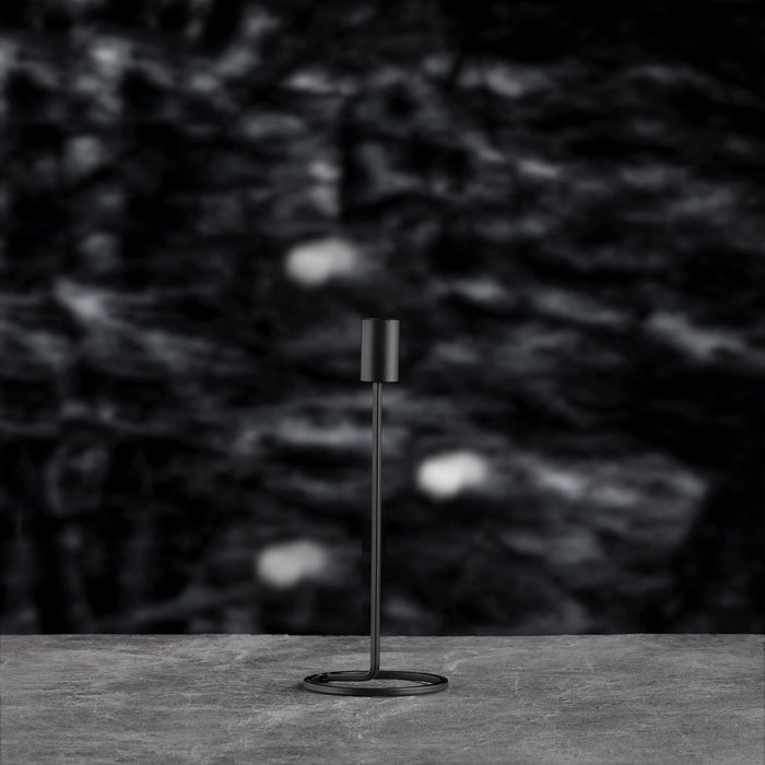 Modern candle holder on a dark surface with a blurred natural background