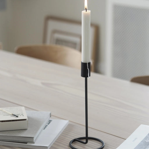 Candle in a black holder on a table with books in the background