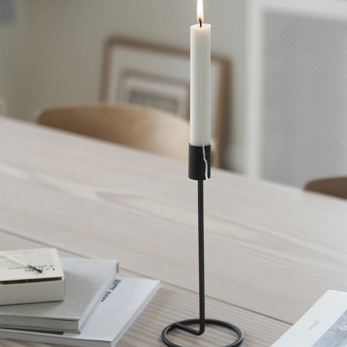 Candle in a black holder on a table with books in the background